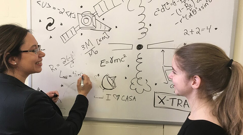 Astrophysicist Julie&nbsp;Hlavacek-Larrondo mentoring high school student Geneviève&nbsp;Sarrazin. They are both in front of a whiteboard filled with physics equations.